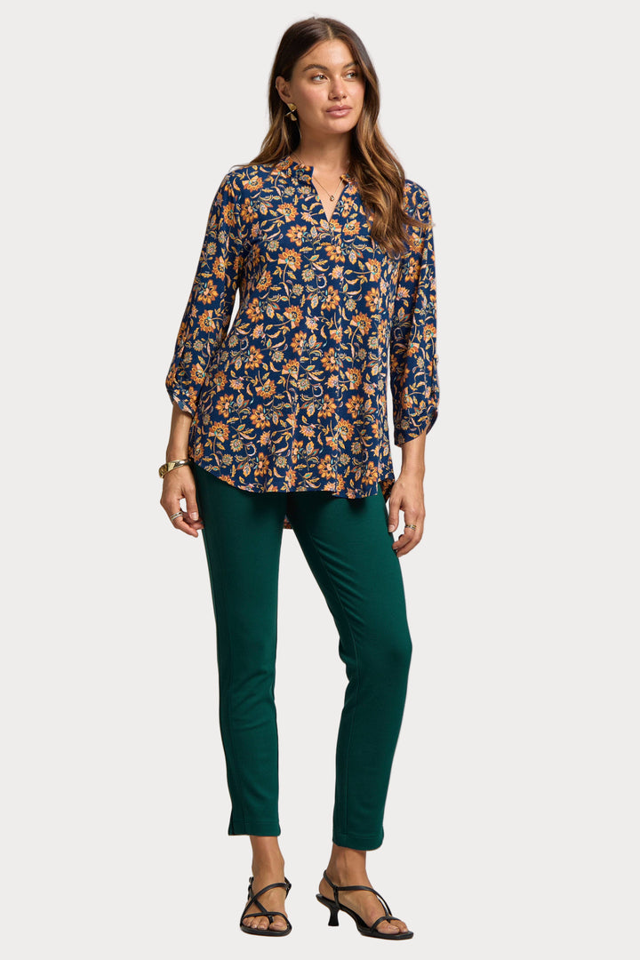 Woman wearing a floral blouse and green pants on a plain background