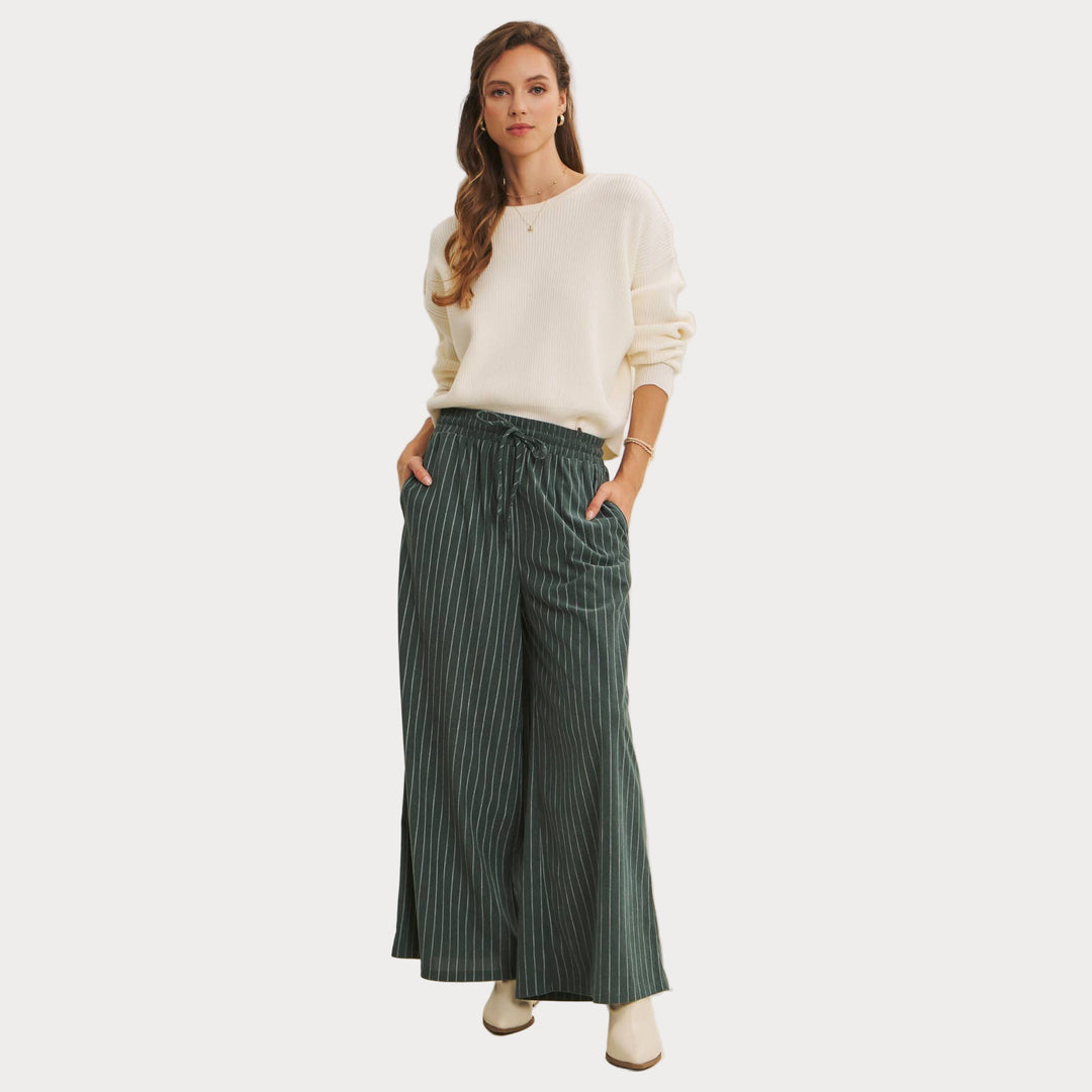 Woman wearing Bow Back Sweater | Dolman Sleeve Knit with Satin Tie styled with green striped pants on a beige background