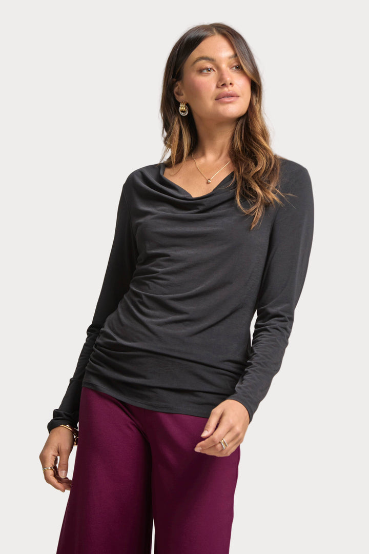 Woman wearing a black long-sleeve top and purple pants on a gray background