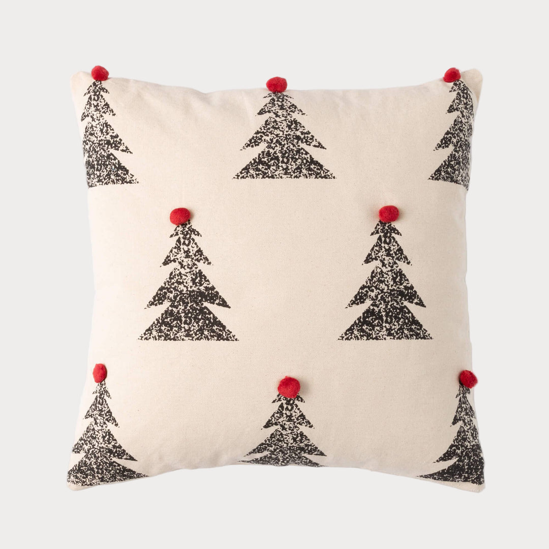Square pillow with black pine tree pattern and red pom poms on neutral fabric background