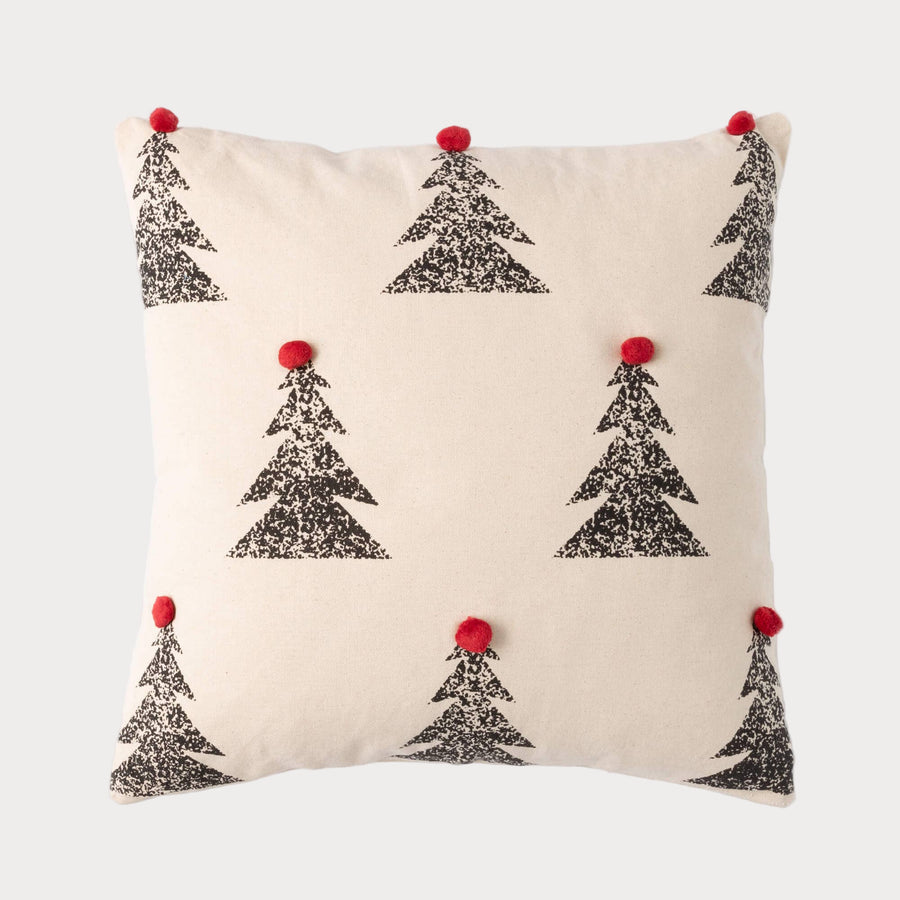 Square pillow with black pine tree pattern and red pom poms on neutral fabric background