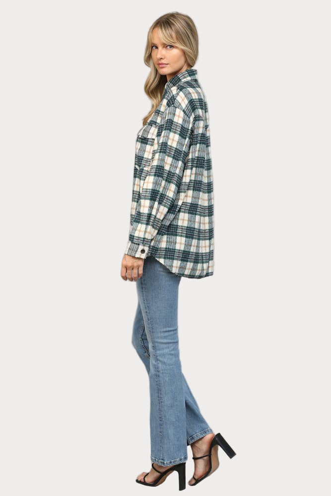 A woman wearing an oversized hunter green, cream, and tan plaid shacket with raw edge chest pockets and snap buttons, paired with light wash jeans.