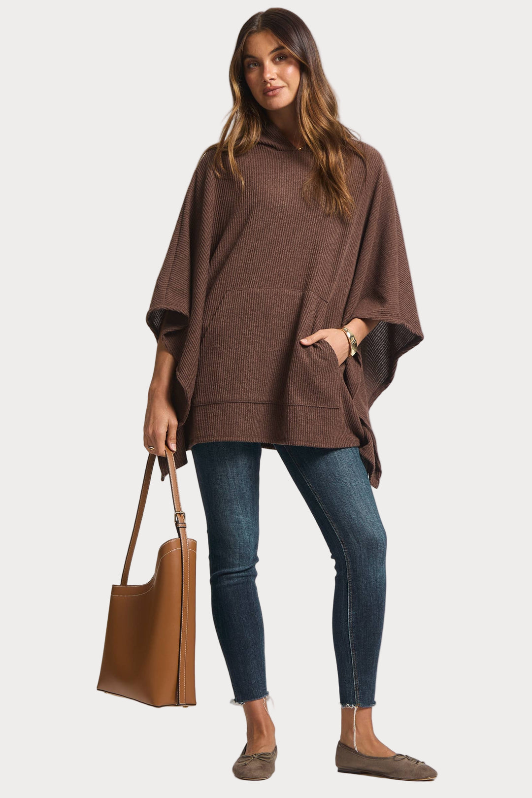 Woman wearing a brown poncho and holding a brown bag on a white background