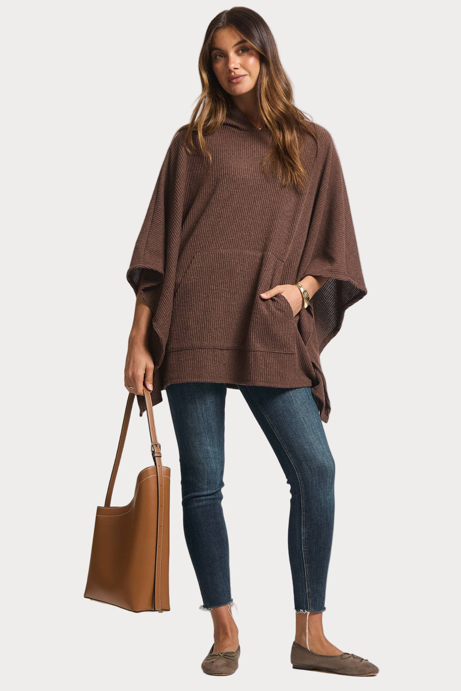 Woman wearing a brown poncho and holding a brown bag on a white background