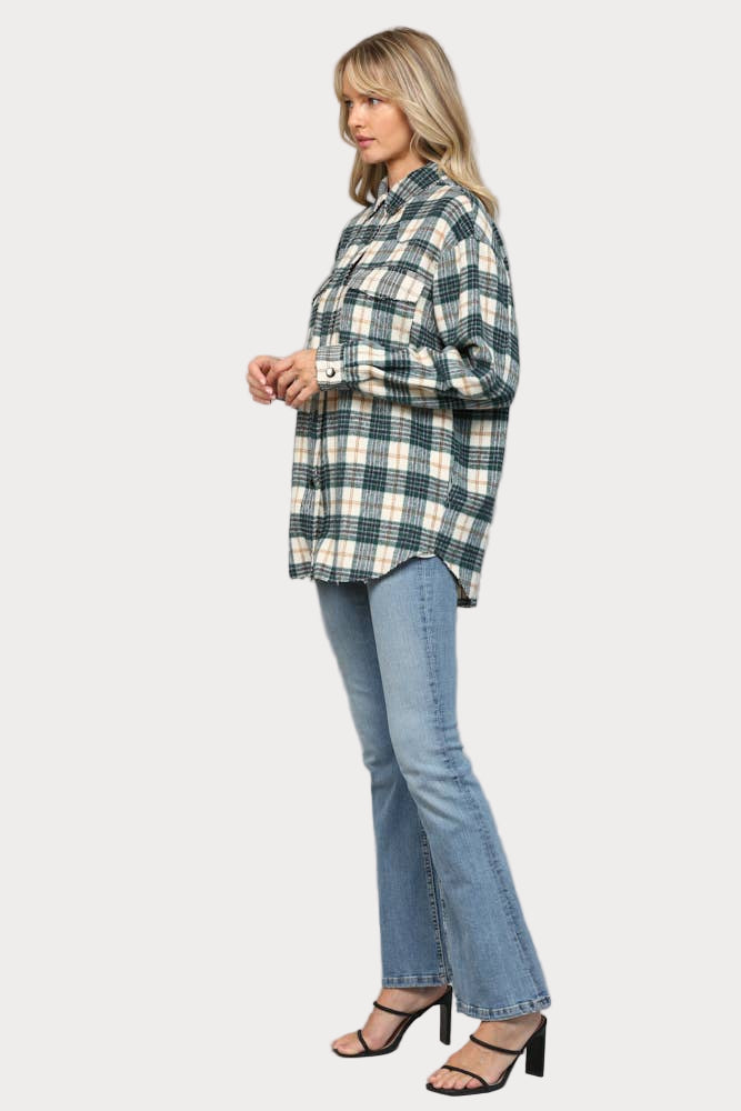 A woman wearing an oversized hunter green, cream, and tan plaid shacket with raw edge chest pockets and snap buttons, paired with light wash jeans.