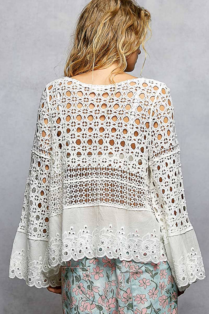 Model wearing The Briar Rose Crochet Blouse featuring intricate open crochet, embroidered eyelet cotton panels, long bell sleeves, and a relaxed bohemian silhouette in ivory.