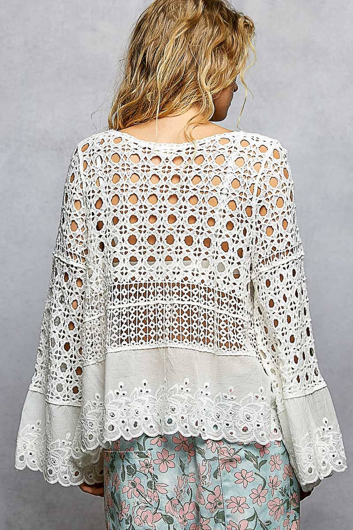 Model wearing The Briar Rose Crochet Blouse featuring intricate open crochet, embroidered eyelet cotton panels, long bell sleeves, and a relaxed bohemian silhouette in ivory.