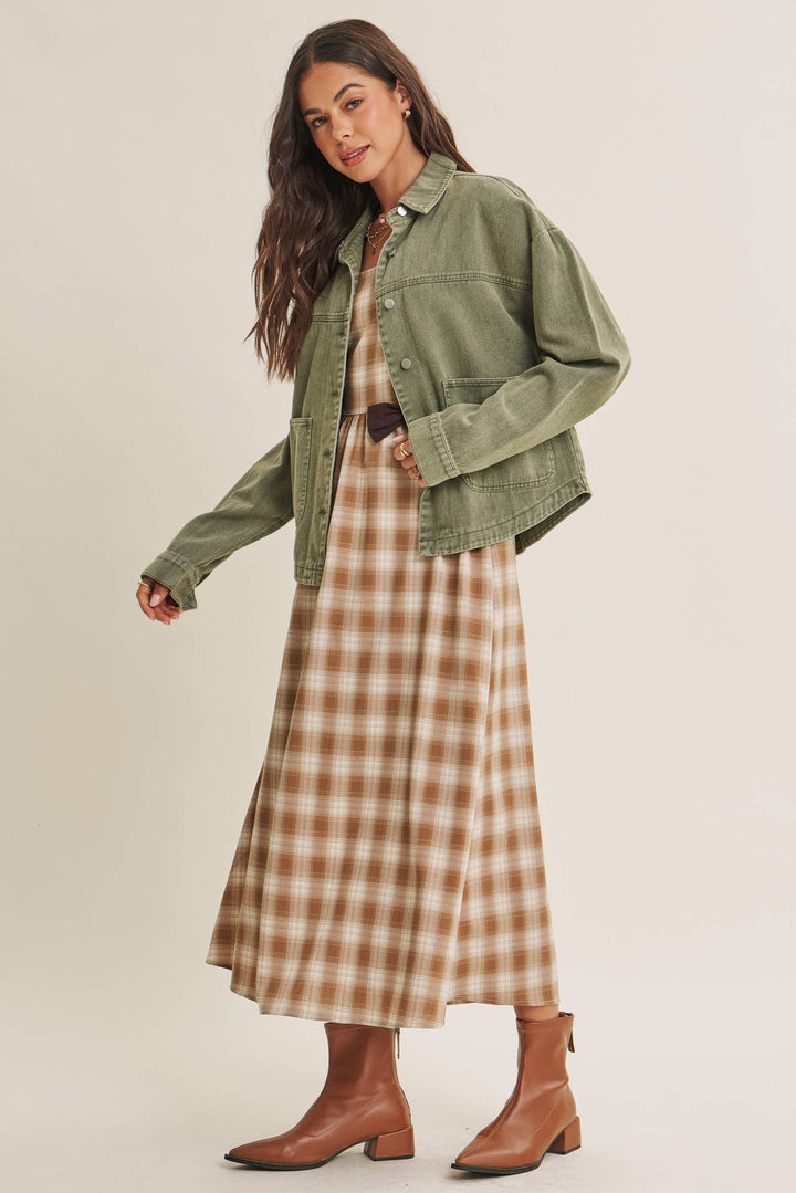Woman wearing a olive green jacket over a plaid dress on a beige background