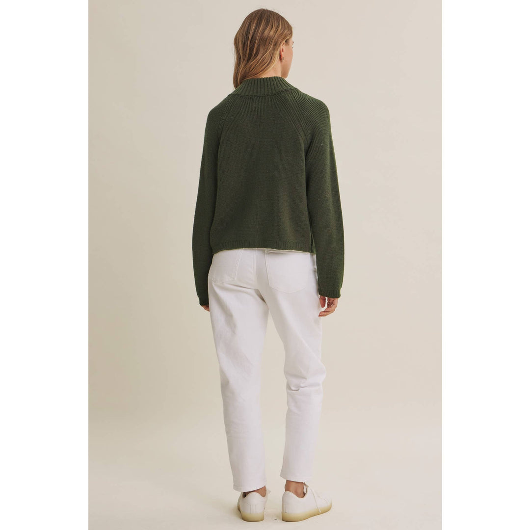 Person wearing a green sweater and white pants on a beige background