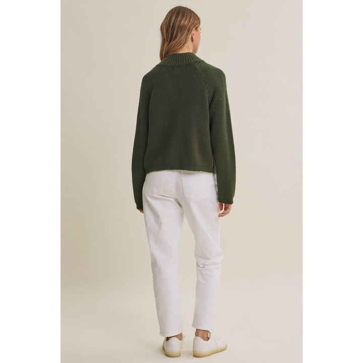 Person wearing a green sweater and white pants on a beige background