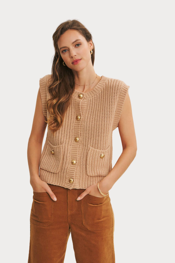 Woman wearing a beige knitted vest with gold buttons on a plain background