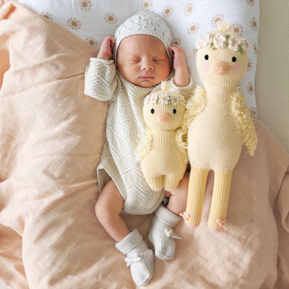 Newborn baby in a knitted outfit with two stuffed knitted duck on a soft surface.