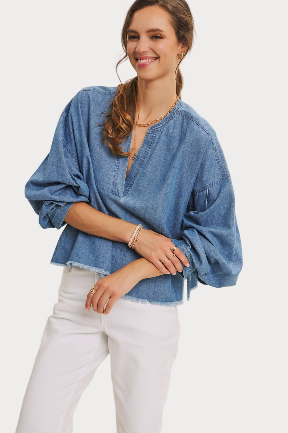 Woman wearing a blue denim top and white pants on a plain background