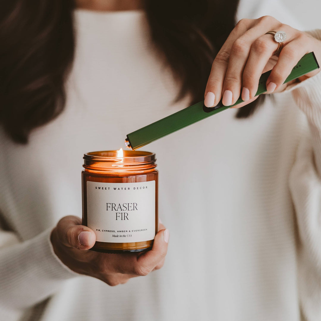 Person lighting a Fraser Fir candle with a green lighter.