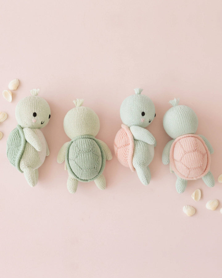 Four knitted turtle toys on a pink background