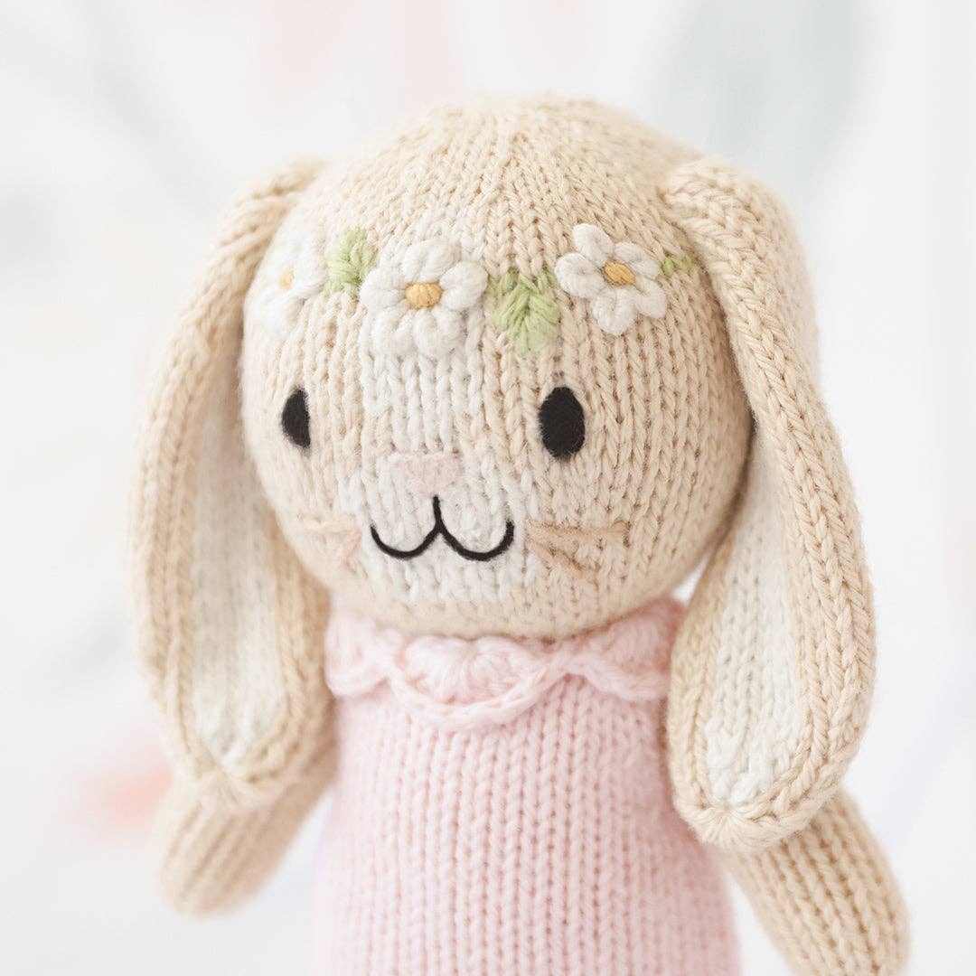 Knitted bunny toy with a pink dress on a light background