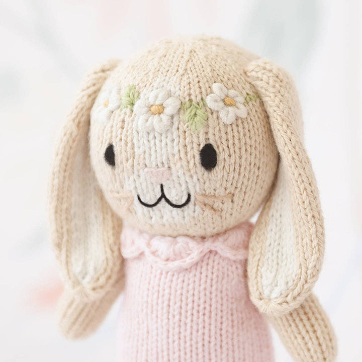Knitted bunny toy with a pink dress on a light background