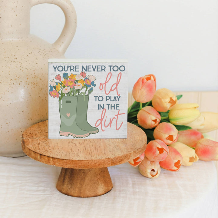 Small sign with floral design and text on a wooden stand with tulips in the background