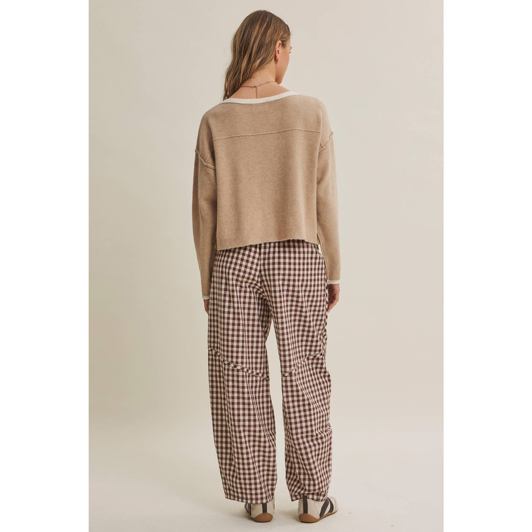 Person wearing a beige sweater and plaid pants on a plain background