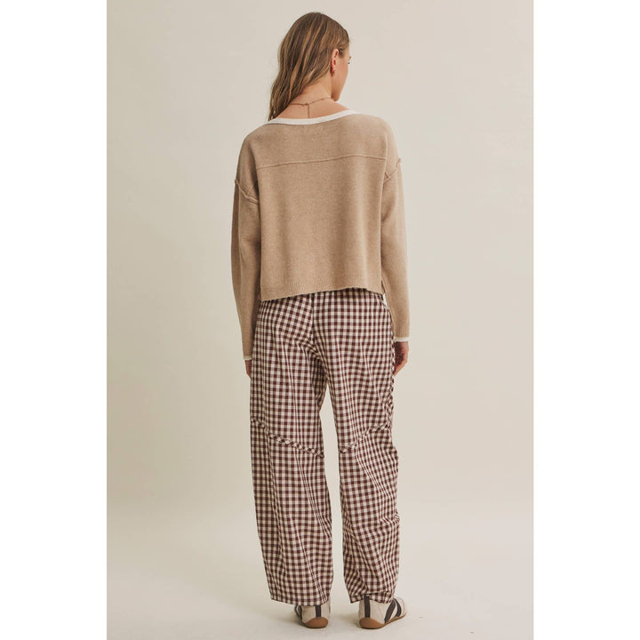 Person wearing a beige sweater and plaid pants on a plain background