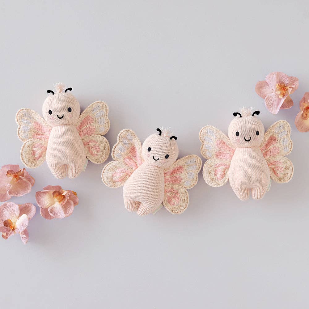 Three knitted butterfly toys with pink wings on a light gray background with pink flowers.