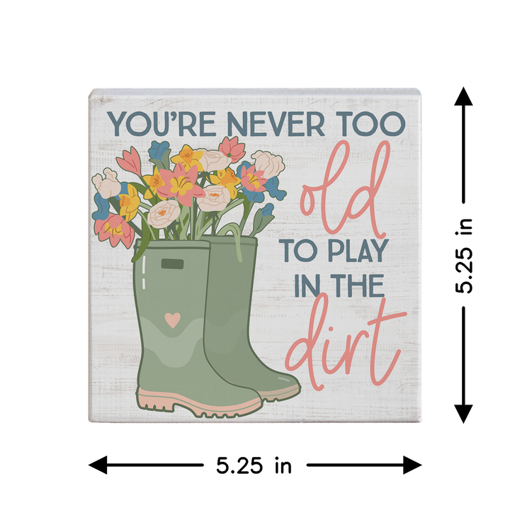 Decorative sign with gardening boots and flowers, featuring text 'You're never too old to play in the dirt'. Showing dimensions.
