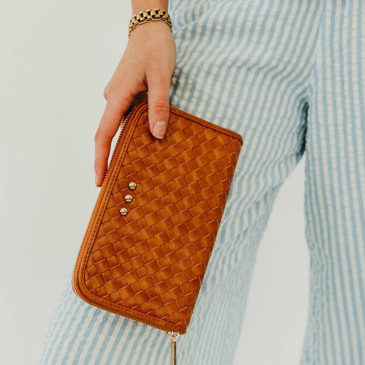 Person holding a brown woven clutch wallet wearing light blue and white striped pants.