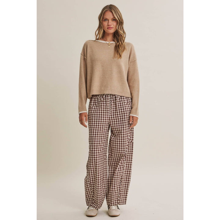 Woman wearing a beige sweater and checkered pants on a plain background