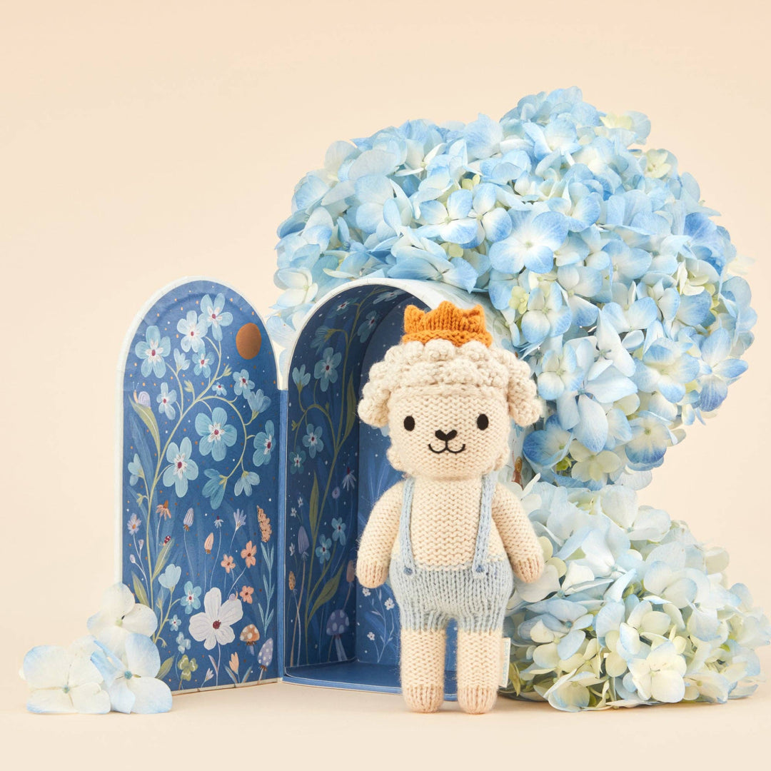 Knitted lamb toy with a blue floral box and hydrangeas on a beige background