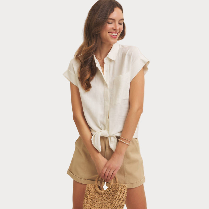 Woman wearing a white shirt and beige shorts holding a woven bag on a beige background