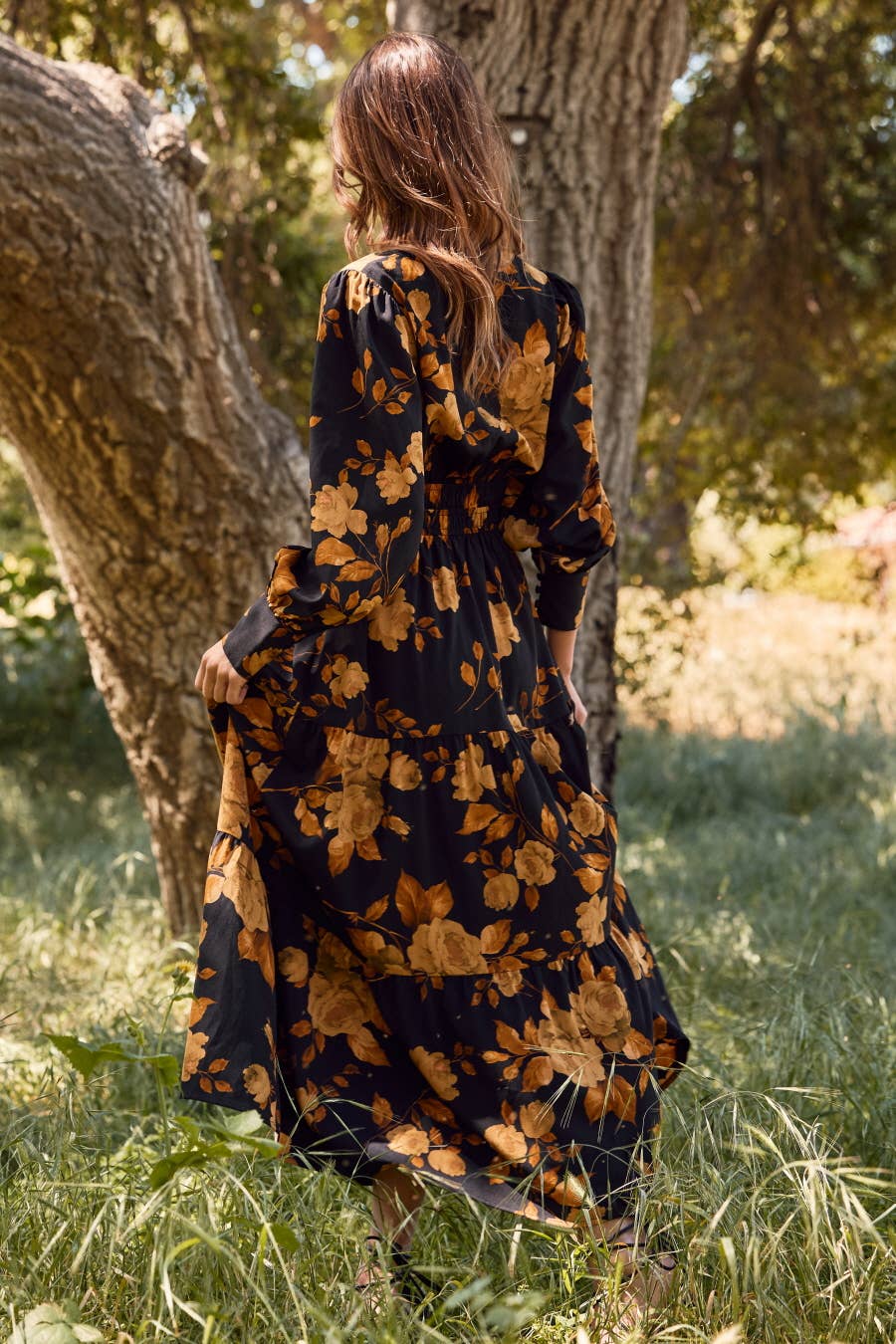 Woman in a black floral dress standing in a grassy area with trees.