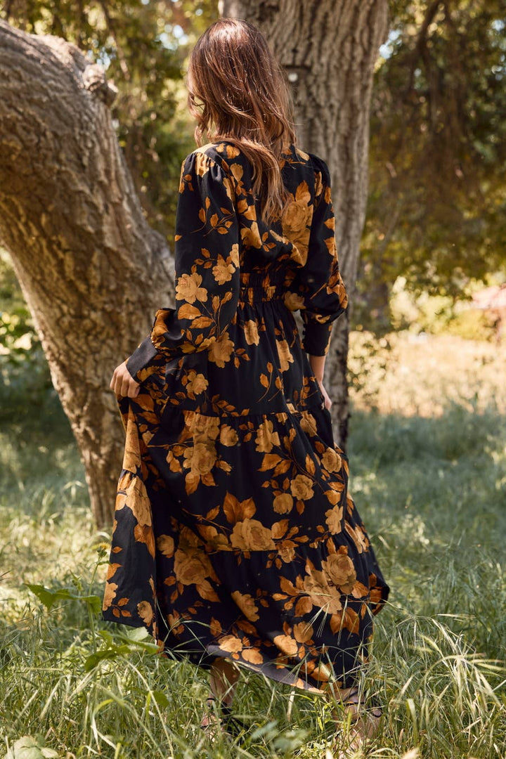 Woman in a black floral dress standing in a grassy area with trees.