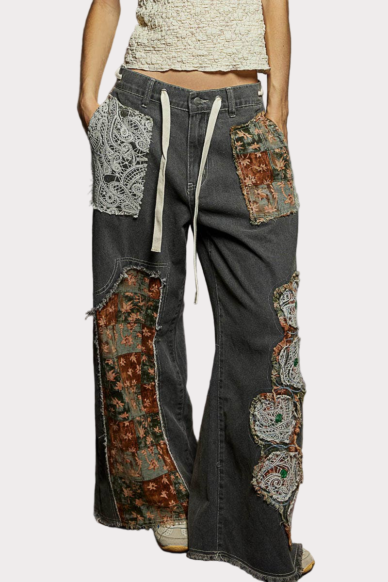 Black denim pants with floral patchwork and lace details, styled with a relaxed wide-leg silhouette.