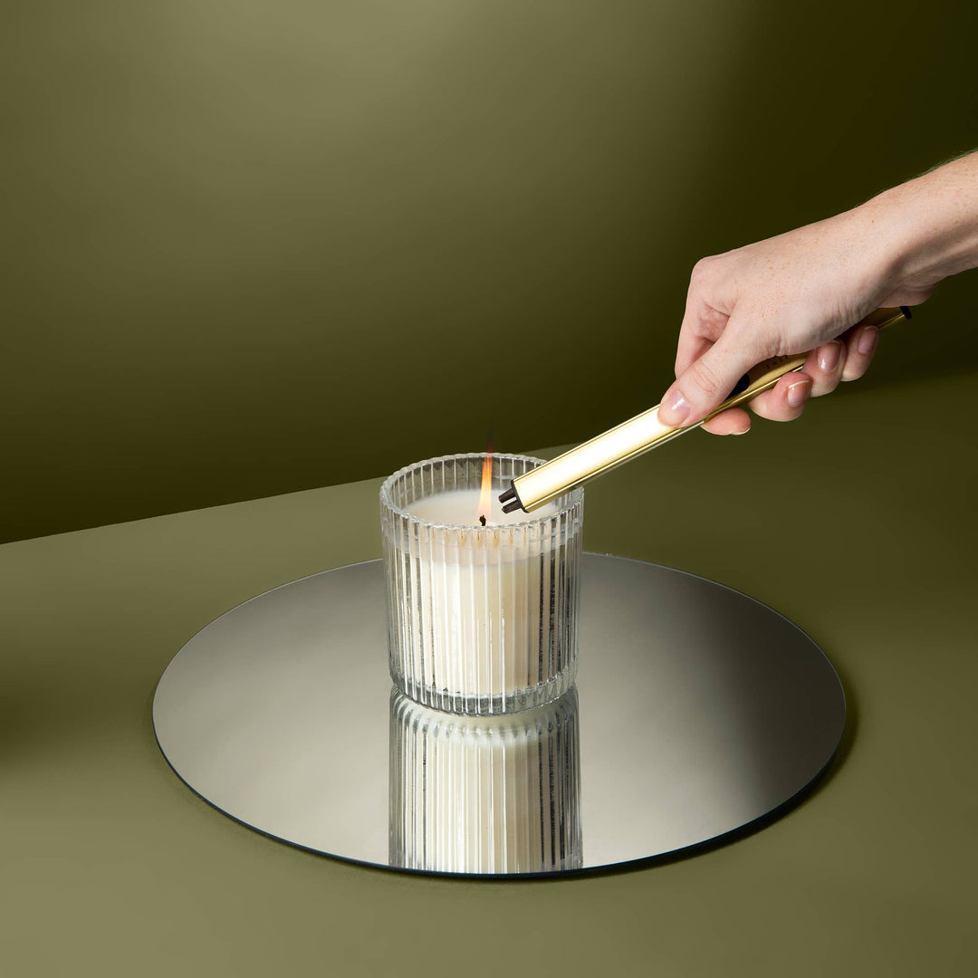 Hand lighting a candle in a glass holder on a reflective surface with a green background