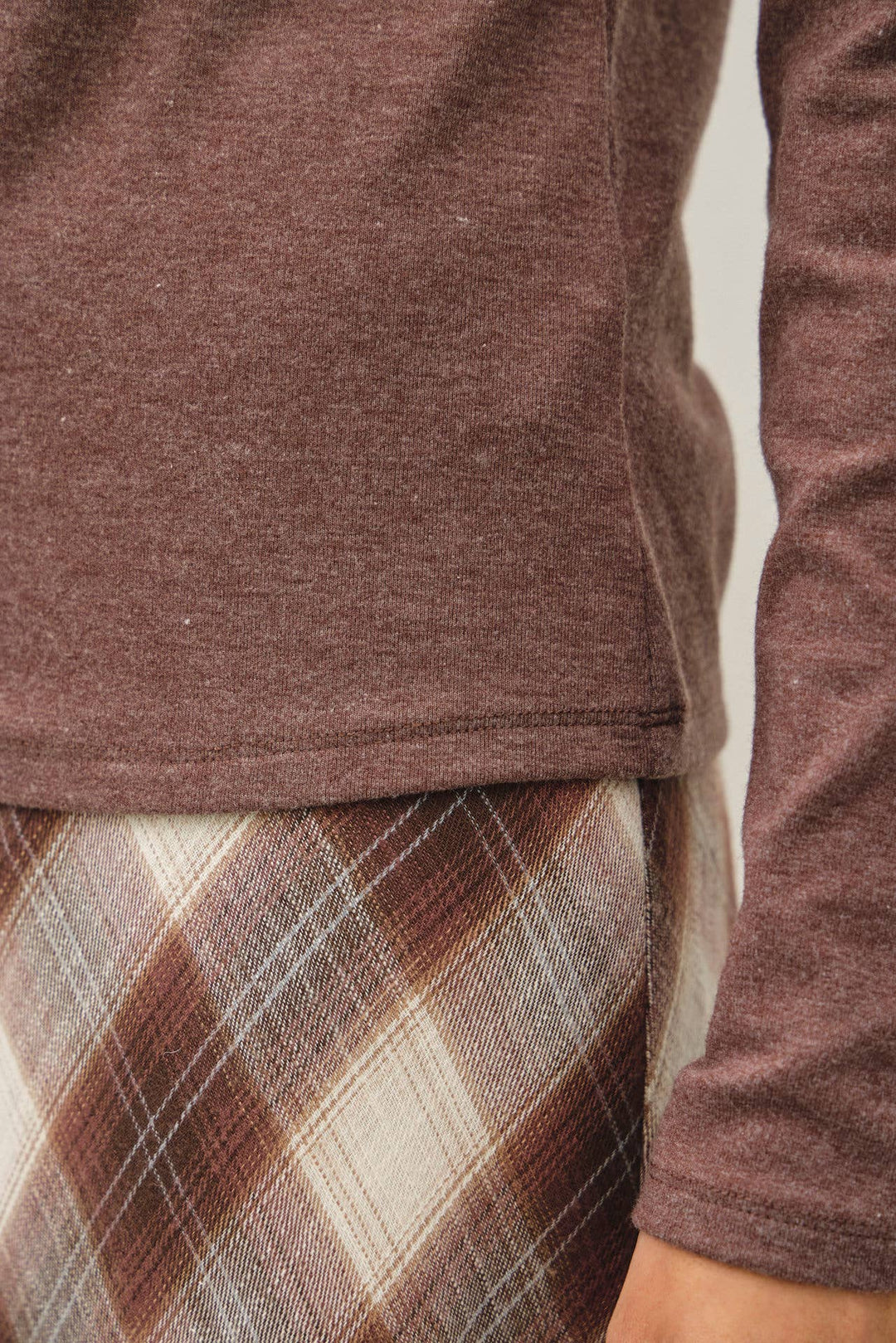 Close-up of a person wearing a heathered brown long-sleeve top and a brown, beige, and gray plaid skirt.