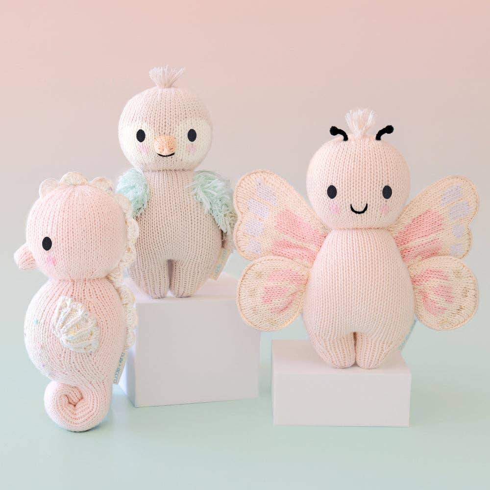 Three knitted toys shaped like a butterfly, seahorse, and bird on a light background