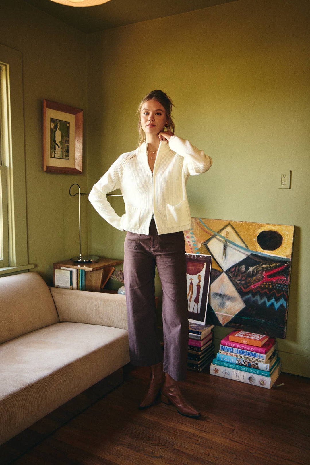 Woman standing in a room with a couch, books, and artwork on the wall.