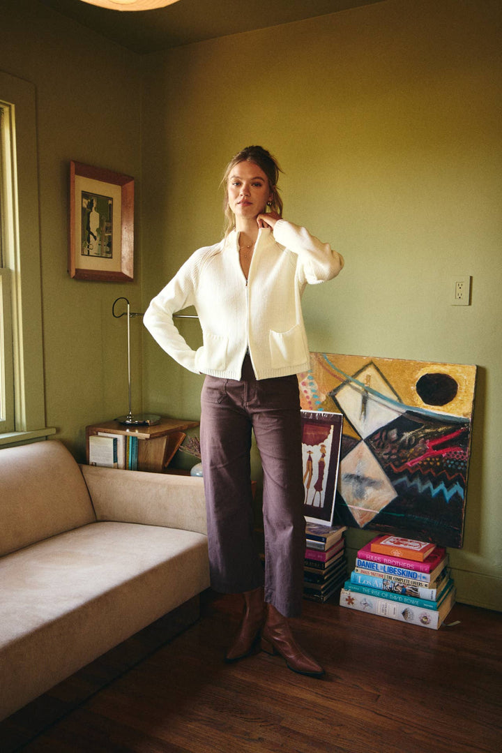 Woman standing in a room with a couch, books, and artwork on the wall.