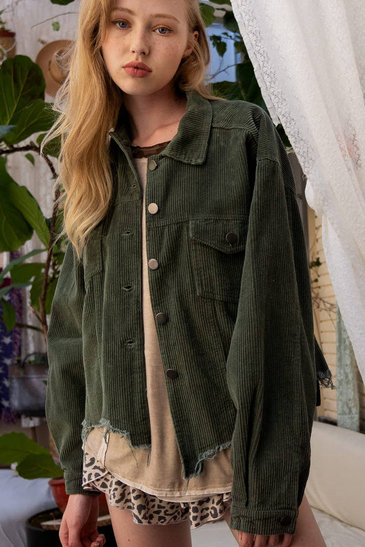 A woman models a relaxed-fit, olive green corduroy jacket with a raw, frayed hem over a tan t-shirt and leopard print shorts.

