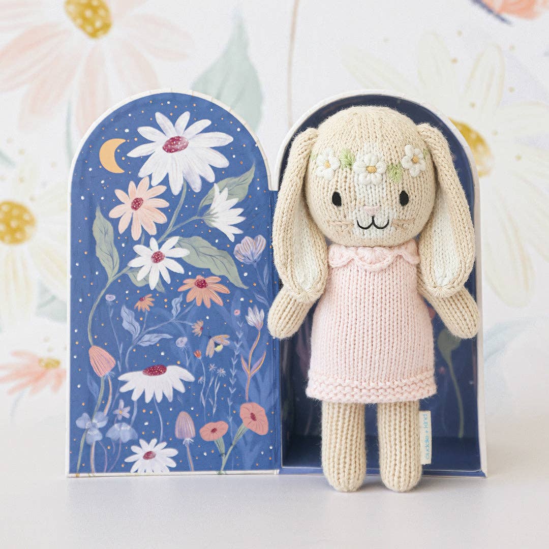 Knitted bunny toy in a pink dress with a floral background