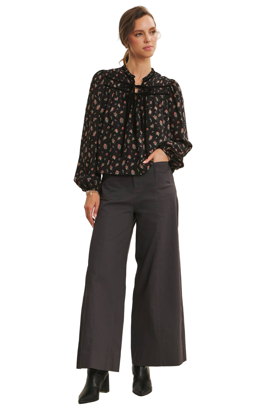 Woman wearing a black floral blouse and gray wide-leg pants on a beige background