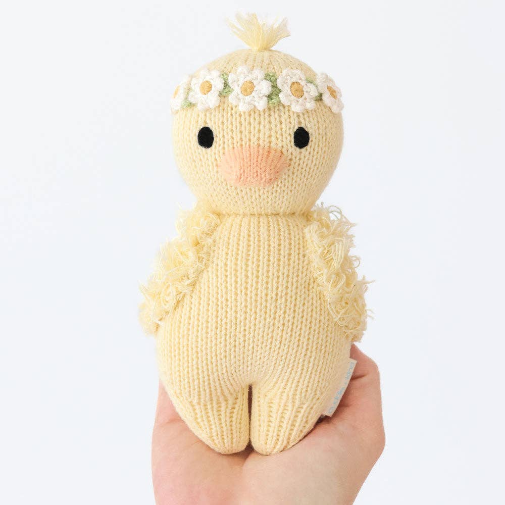 Knitted toy duck with a flower crown held in a hand against a white background