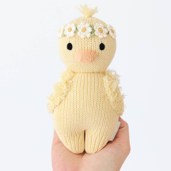 Knitted toy duck with a flower crown held in a hand against a white background