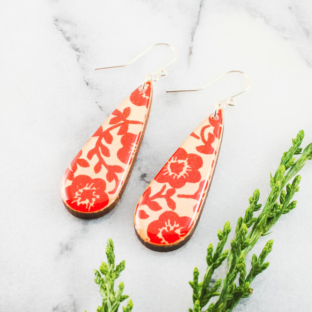 Teardrop-shaped earrings with red floral pattern on a light background