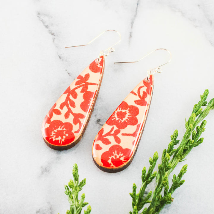 Teardrop-shaped earrings with red floral pattern on a light background