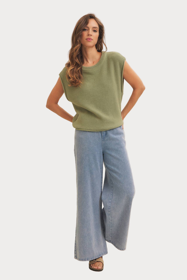 Woman wearing a green sleeveless top and blue jeans on a white background