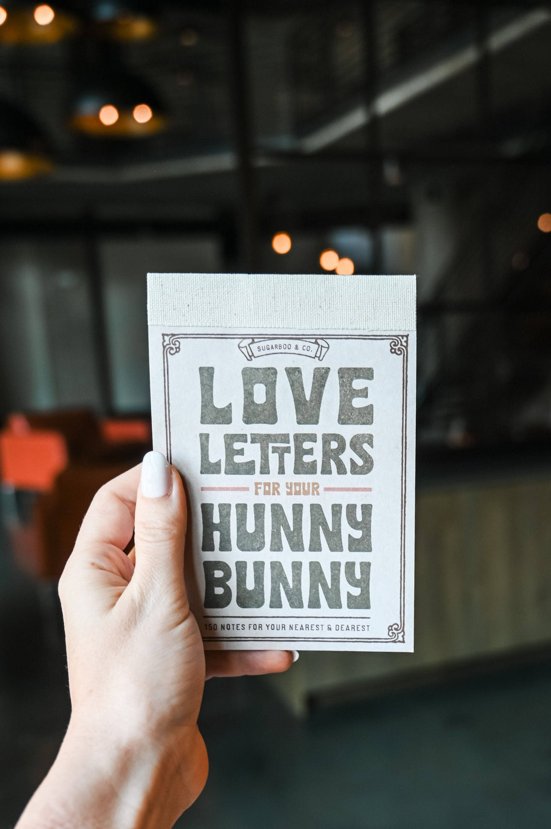 Hand holding a card with 'Love Letters for Your Hunny Bunny' text against a blurred indoor background.