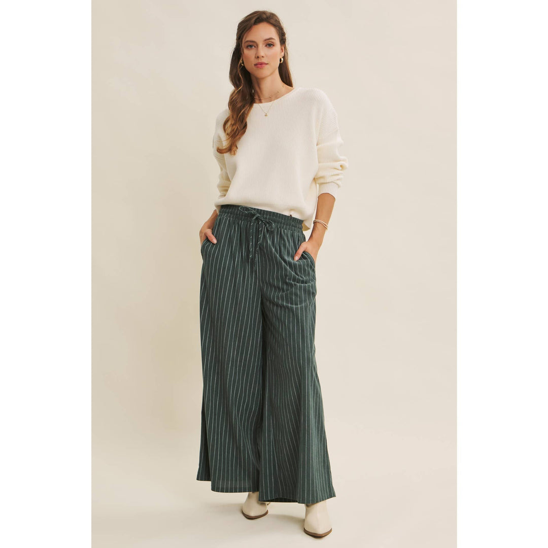 Woman wearing Bow Back Sweater | Dolman Sleeve Knit with Satin Tie styled with green striped pants on a beige background