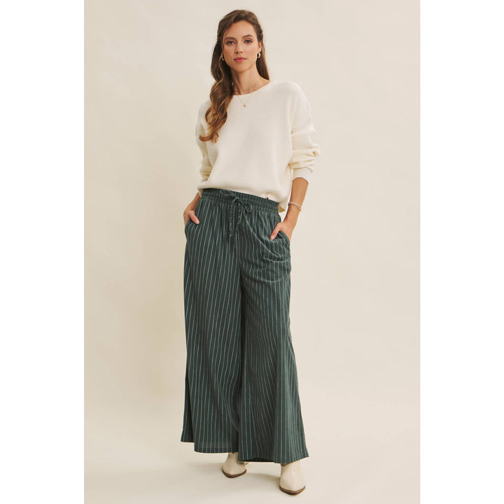 Woman wearing Bow Back Sweater | Dolman Sleeve Knit with Satin Tie styled with green striped pants on a beige background
