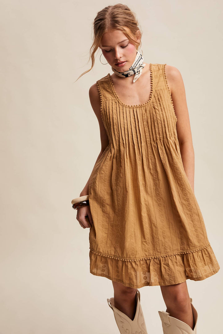 Woman wearing a textured camel-colored sleeveless mini dress with pintuck details and ruffle hem.